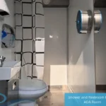 Interior of ADA restroom trailer with toilet, sink, shower curtain, and mounted toilet paper dispenser