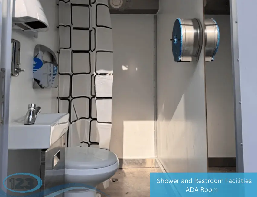 Interior of ADA restroom trailer with toilet, sink, shower curtain, and mounted toilet paper dispenser