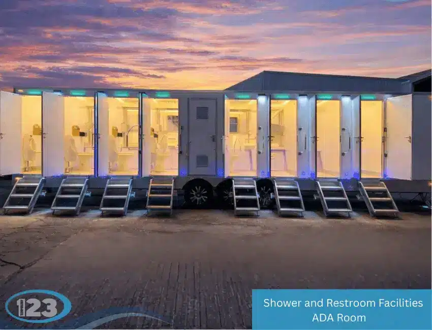 Large illuminated shower and restroom trailer with multiple open stalls, interior lighting, steps, and accessible entry at sunset
